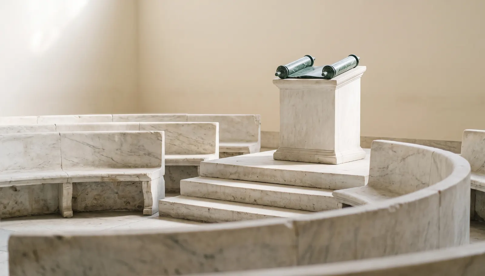 A marble bema: steps up to a lectern with a green marble scroll open on it, empty stone benches curving around it